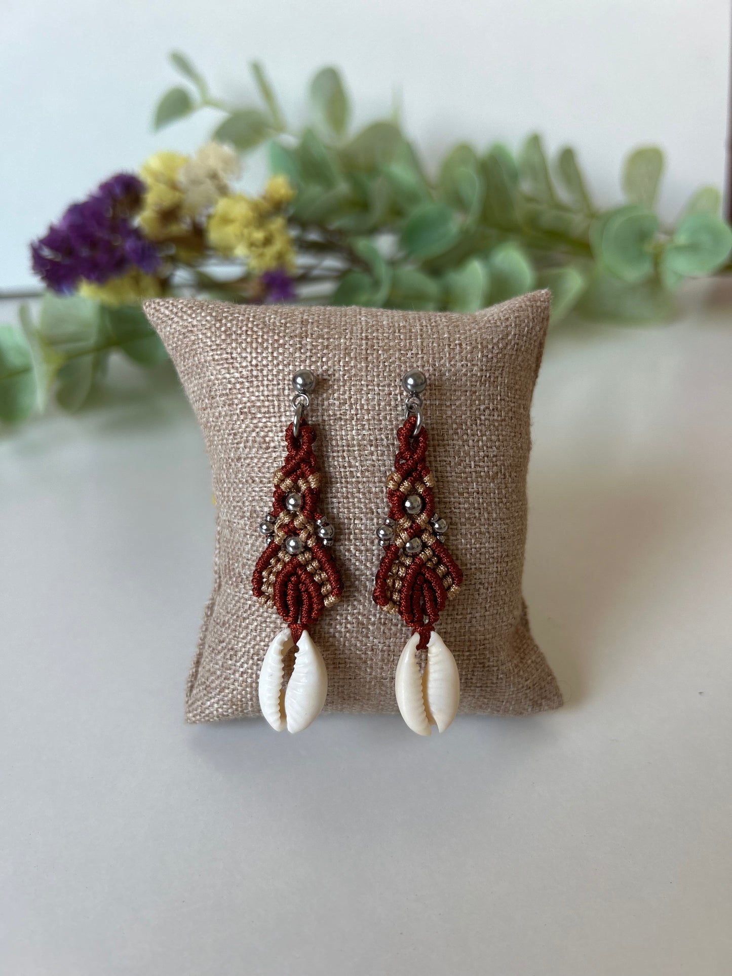 Sumérgete en la belleza del mar con los pendientes Ola Marina, una pieza única que captura la esencia de la costa. Estos pendientes están meticulosamente elaborados con hilo de nailon, conchas naturales y cuentas de acero inoxidable, utilizando la técnica de macramé para ofrecerte un accesorio sofisticado y lleno de estilo.