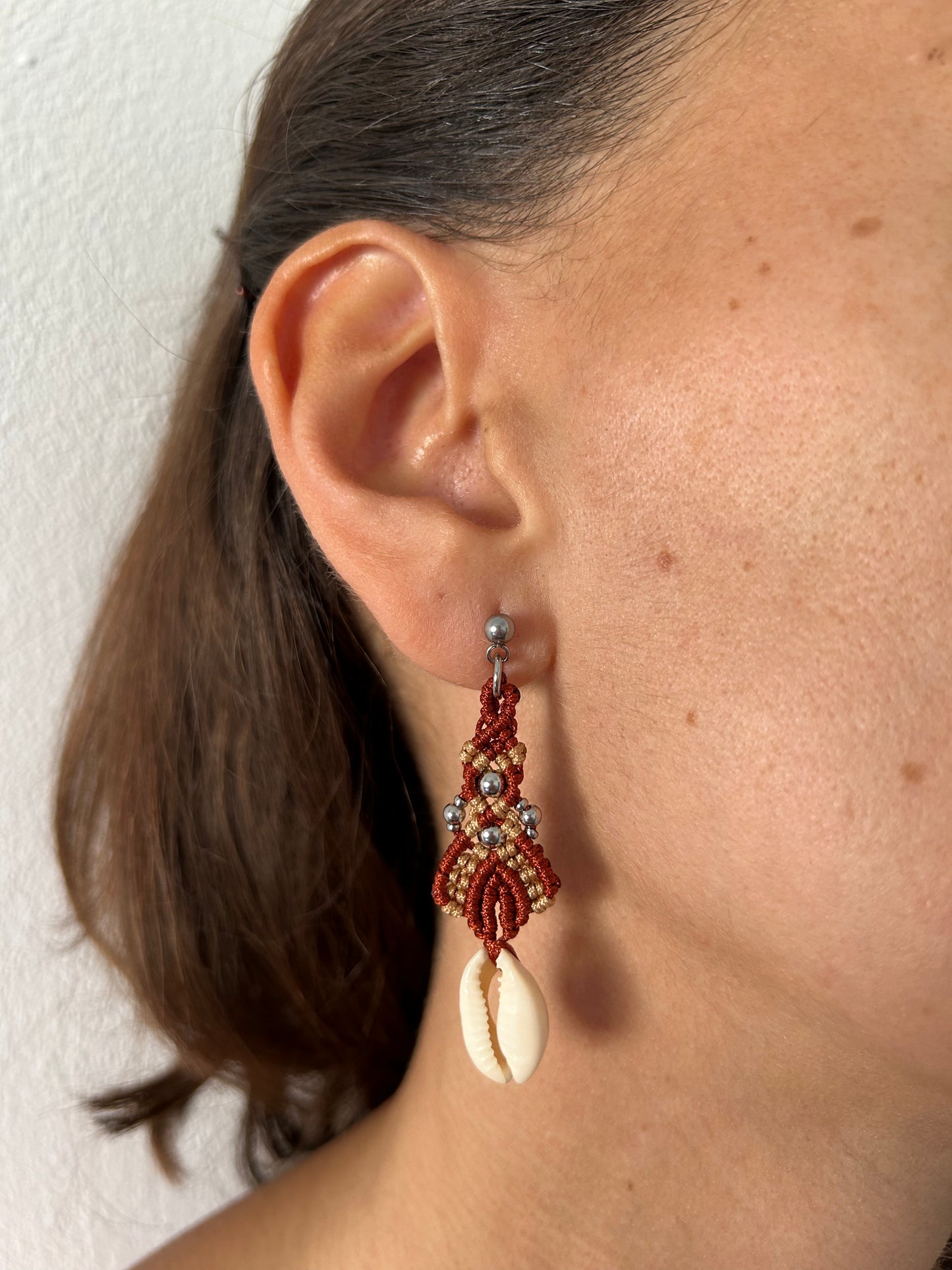 Sumérgete en la belleza del mar con los pendientes Ola Marina, una pieza única que captura la esencia de la costa. Estos pendientes están meticulosamente elaborados con hilo de nailon, conchas naturales y cuentas de acero inoxidable, utilizando la técnica de macramé para ofrecerte un accesorio sofisticado y lleno de estilo.