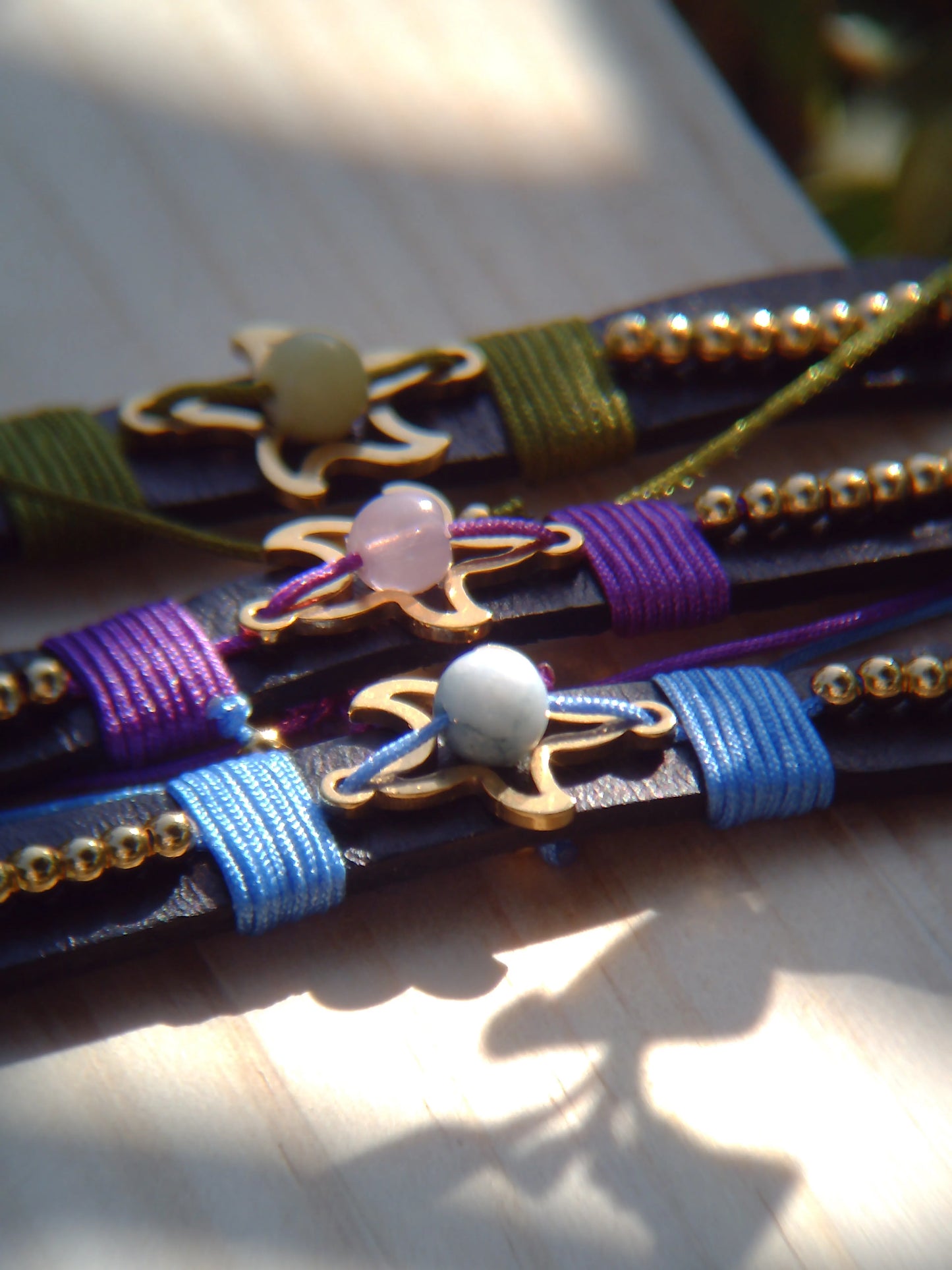 Pulseras artesanales de cuero sintético con hilos de nailon y charms de acero inoxidable. Resistentes, ajustables y disponibles en varios colores.