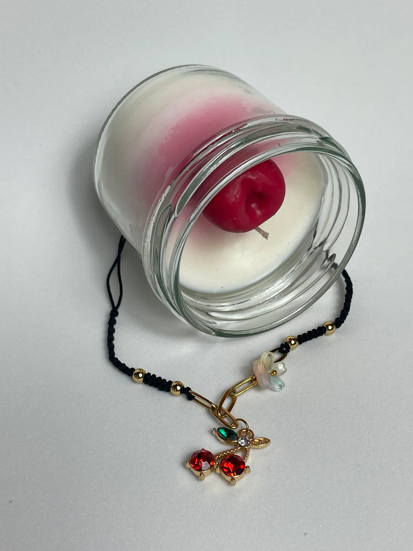 Pack Cereza: vela artesanal de soja con aroma a cereza y pulsera de macramé con charm de cereza en acero inoxidable y cristales facetados.