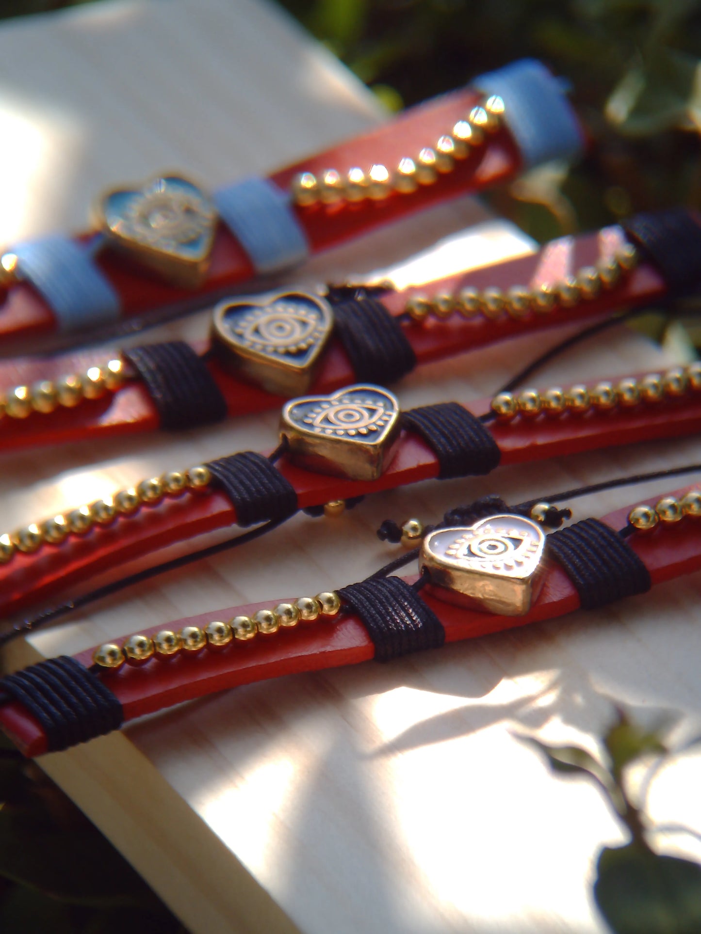 Pulseras artesanales de cuero sintético con hilos de nailon y charms de acero inoxidable. Resistentes, ajustables y disponibles en varios colores.