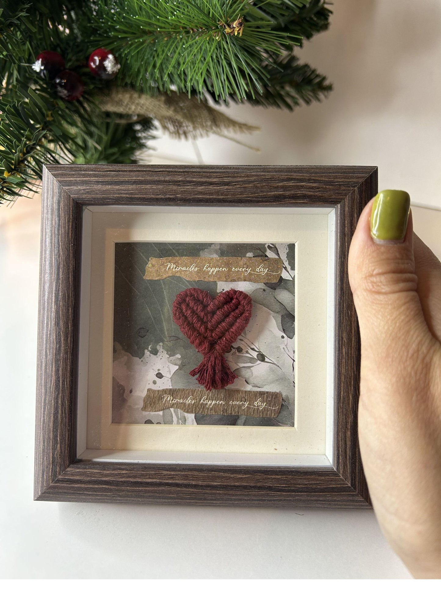 Persona sosteniendo el mini cuadro de macramé para mostrar su tamaño real. Detalle del arte en macramé y el diseño del marco de fotos.