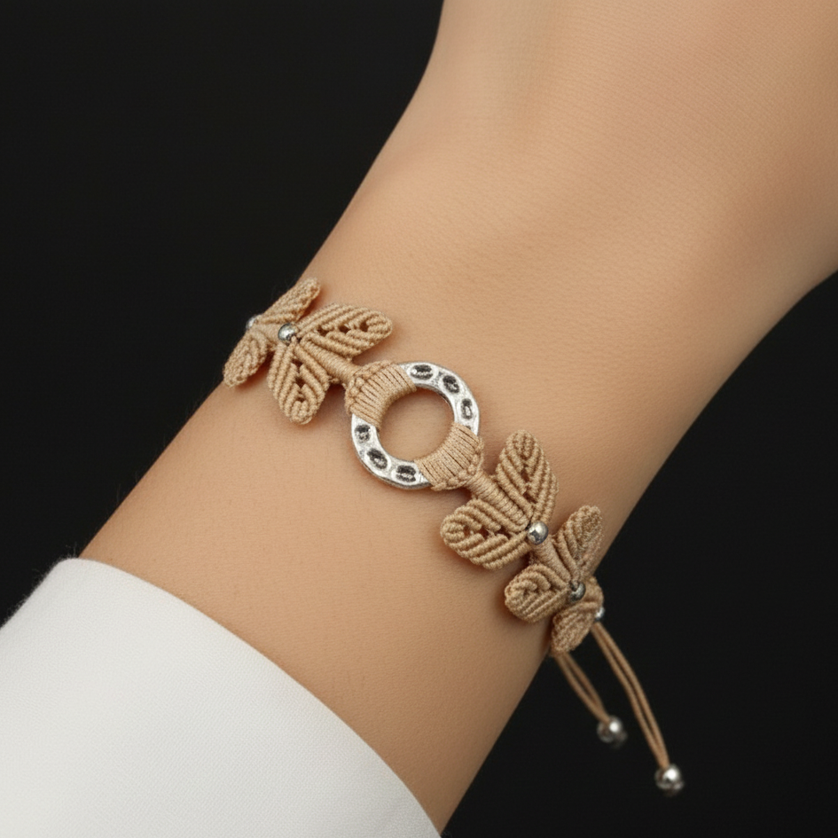 Brazalete artesanal de macramé en beige con pieza central circular metálica y cierre ajustable.