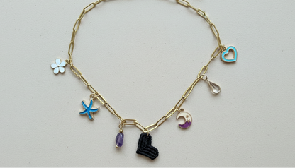 Collar dorado con charms variados en forma de corazón negro tejido, charms de acero. Tendencia 2026