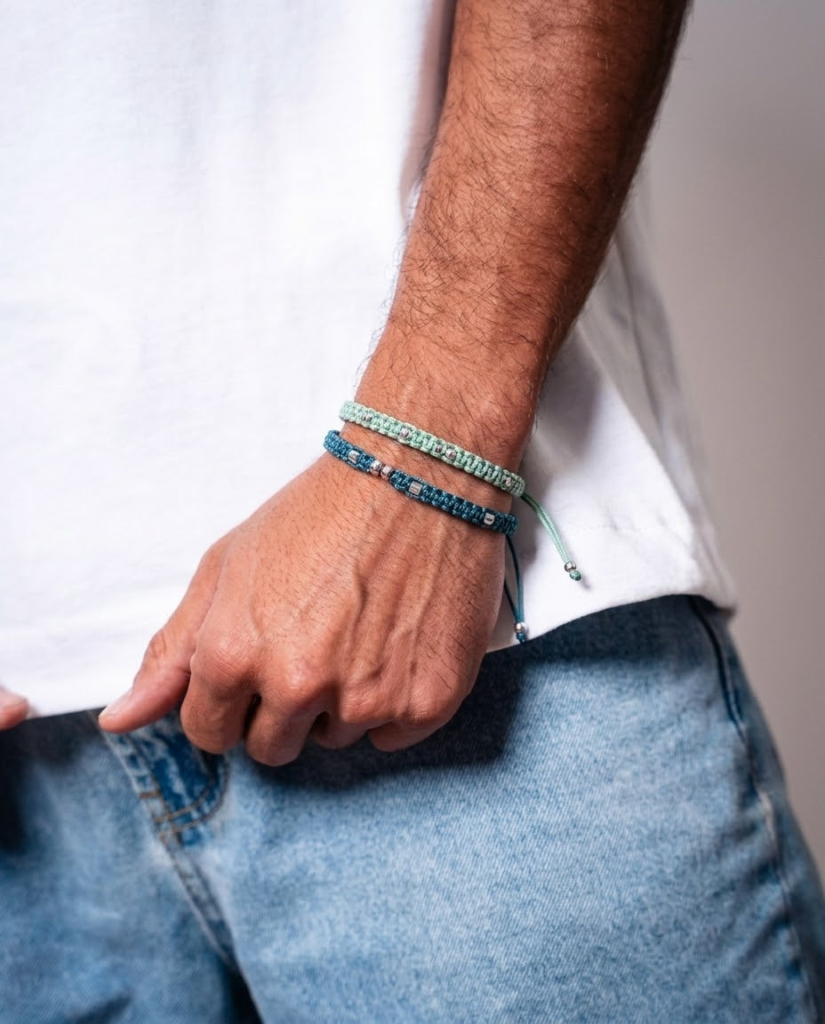 Hombre con pulseras dobles de cordón trenzado verde menta y azul petróleo con cuentas metálicas, combinadas con camiseta blanca y vaqueros