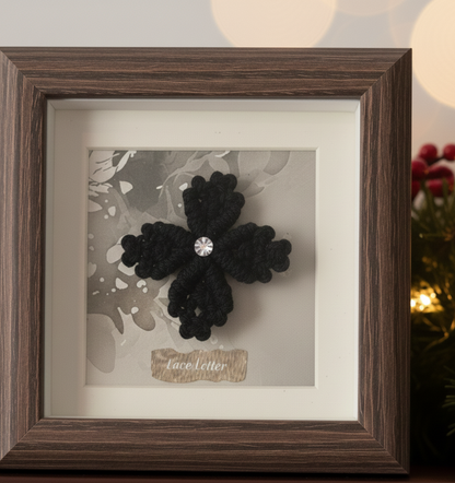Detalle de mini cuadro con flor de macramé negra. Marco de madera y fondo sutil acuarela, perfecto para regalo de navidad o detalle decorativo.