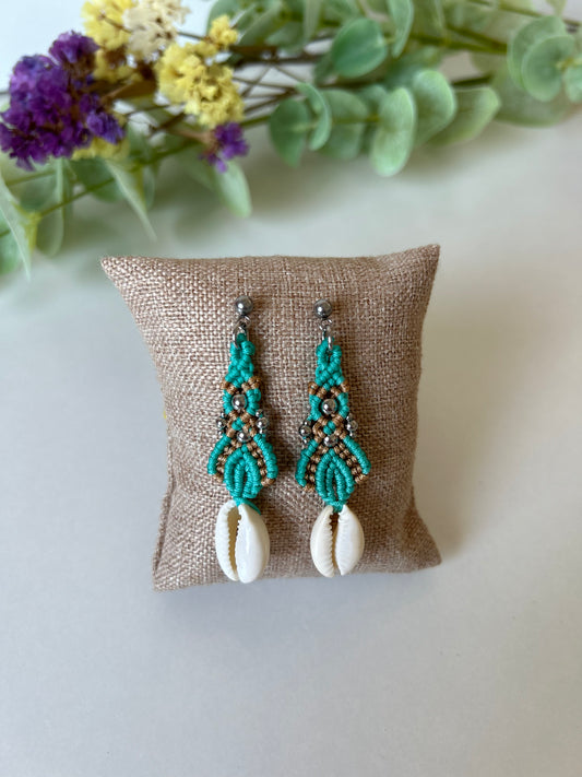 Sumérgete en la belleza del mar con los pendientes Ola Marina, una pieza única que captura la esencia de la costa. Estos pendientes están meticulosamente elaborados con hilo de nailon, conchas naturales y cuentas de acero inoxidable, utilizando la técnica de macramé para ofrecerte un accesorio sofisticado y lleno de estilo.