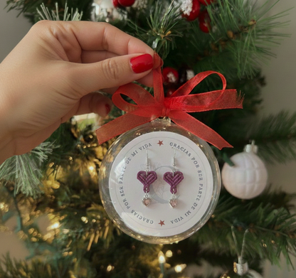 Esfera de regalo navideña con la frase "Gracias por ser parte de mi vida", conteniendo los pendientes de corazón.