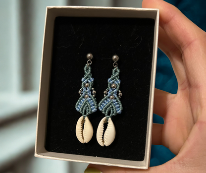 Sumérgete en la belleza del mar con los pendientes Ola Marina, una pieza única que captura la esencia de la costa. Estos pendientes están meticulosamente elaborados con hilo de nailon, conchas naturales y cuentas de acero inoxidable, utilizando la técnica de macramé para ofrecerte un accesorio sofisticado y lleno de estilo.