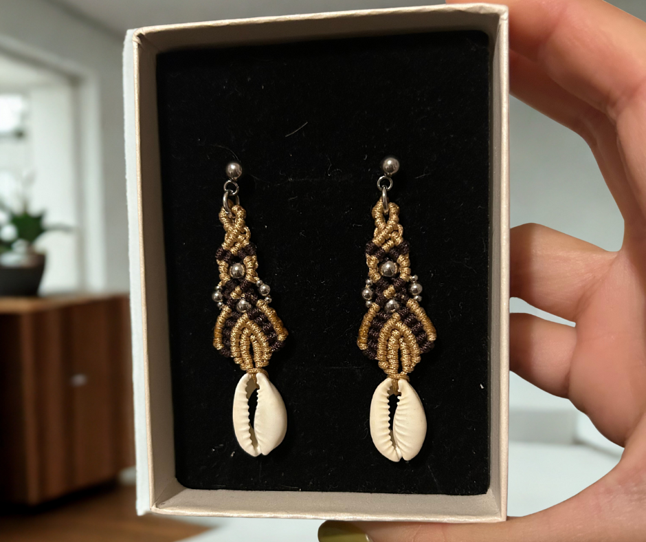 Sumérgete en la belleza del mar con los pendientes Ola Marina, una pieza única que captura la esencia de la costa. Estos pendientes están meticulosamente elaborados con hilo de nailon, conchas naturales y cuentas de acero inoxidable, utilizando la técnica de macramé para ofrecerte un accesorio sofisticado y lleno de estilo.