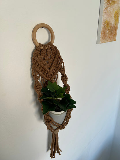Transforma tu espacio con el Portamacetas Brown, una pieza única que combina la belleza natural con la artesanía moderna. Este portamacetas está meticulosamente diseñado utilizando la técnica de macramé sobre una base de madera en forma de aro, creando un accesorio elegante y funcional para tus plantas favoritas.