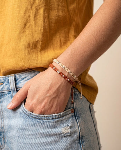 Pulseras trenzadas ajustables en tonos crudo y terracota con cuentas plateadas, estilo boho combinadas con vaqueros
