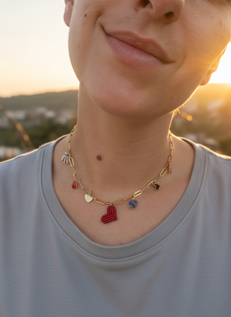 Collar dorado con charms de colores en forma de corazón, concha y piedra azul mostrado en el cuello, fotografía lifestyle al atardecer.