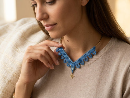 Mujer tocando su collar de macramé azul con piedra y colgante dorado sobre jersey beige